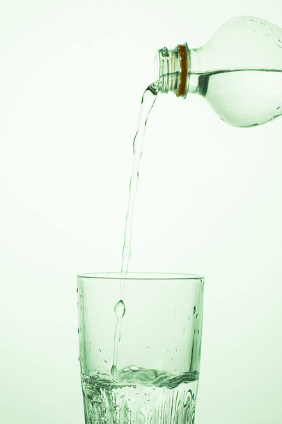 Um homem derrama água de uma garrafa de plástico transparente em um copo - Foto, Imagem