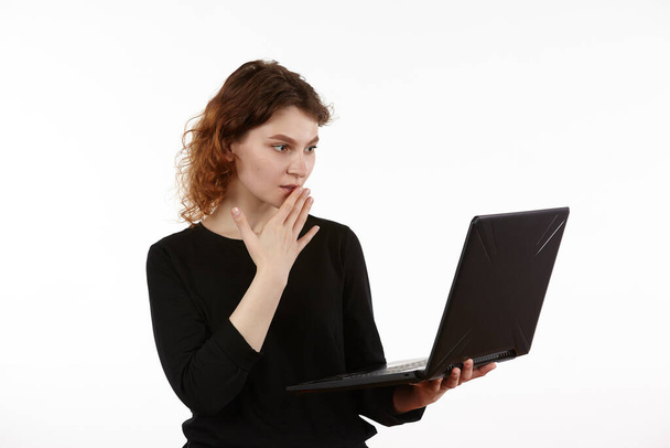 A young slender girl in black clothes works on a laptop. Figure isolated on a white background. - Photo, image