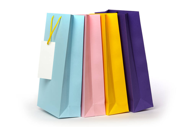 Quatre sacs d'emballage multicolores avec poignées et étiquette blanche isolés sur fond blanc. - Photo, image