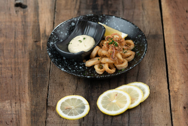 Assiette de calamars frits croustillants, calamars au poivron rouge fumé, amande, vinaigre de cerise, tomate et cayenne servie avec sauce tartare sur le côté isolé sur une table en bois - Photo, image