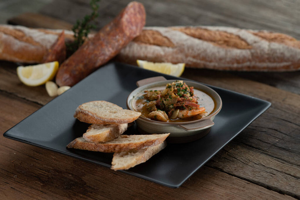 Gambas Pil Pil - Crevettes pétillantes au chili et à l'ail servies avec du pain sur le côté isolé sur une table rustique en bois - Photo, image