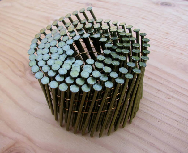 Coil nails in roll for nailer guns on plywood background. - Photo, Image