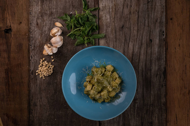 Top view of homemade gnocchi with pesto sauce, parmesan and basil isolated on wooden table - Foto, Imagem