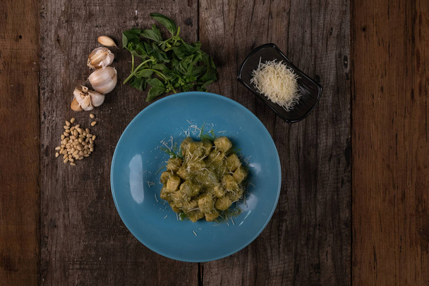 Top view of homemade gnocchi with pesto sauce, parmesan and basil isolated on wooden table - Foto, afbeelding
