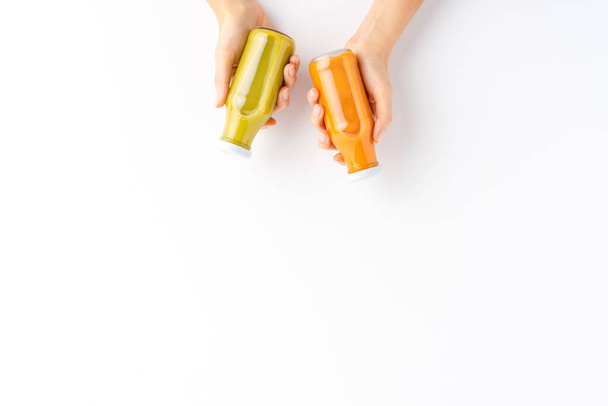 Female hands holding bottles of fruit and vegetable smoothies isolated on white background with copyspace. Top view - Foto, Bild