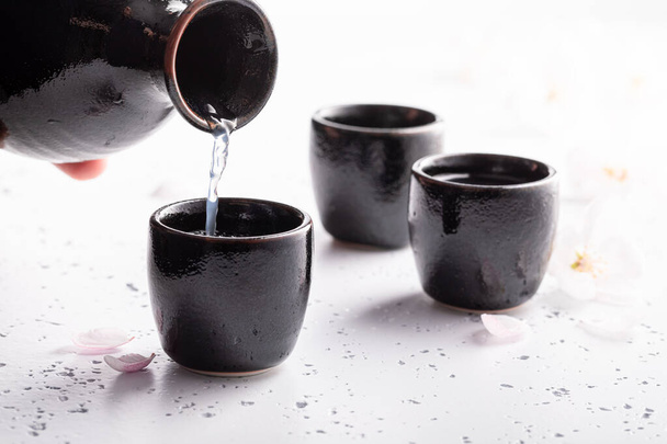 Japanese sake with blooming cherry. Traditionally served sake in ceramics. Black ceramics on a white stone. - Foto, afbeelding