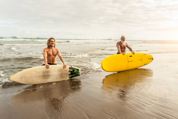 Amigos felices con diferentes edades surfeando juntos - Gente deportiva divirtiéndose durante el día de surf de vacaciones - Concepto de estilo de vida de deporte extremo - Foto, Imagen