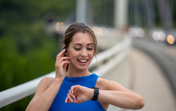 Young athlete exercising outdoors on bridge. Runner using smart watch for health data and statistics. - Photo, Image