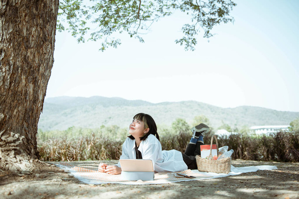 Picknickkonzept ein Smiley-Mädchen mit kurzen Haaren, das auf der Karte liegt und mit seinem Tablet im Picknickbereich genießt. - Foto, Bild