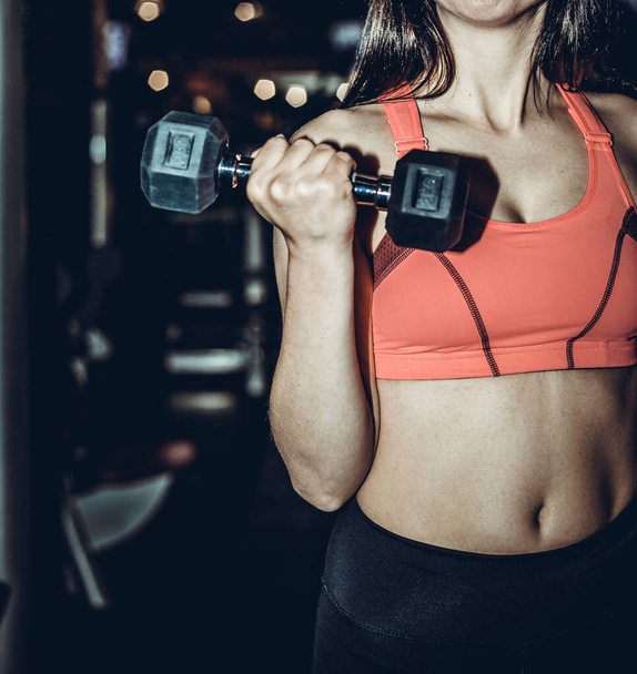 Fitness sporty woman in training pumping up muscles with dumbbells. Young sports sexy fitness woman body with dumbbells posing on dark background. - Foto, Bild
