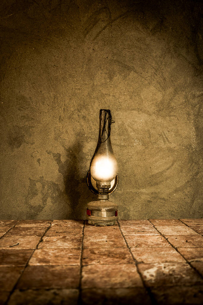Vecchia, antica lampada ad olio che brucia su piastrelle rustiche con sfondo muro di cemento. Elettrodomestici vintage. Con spazio di copia. - Foto, immagini