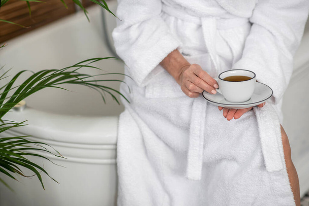 Woman in a white robe holding a cup with tea - Foto, imagen