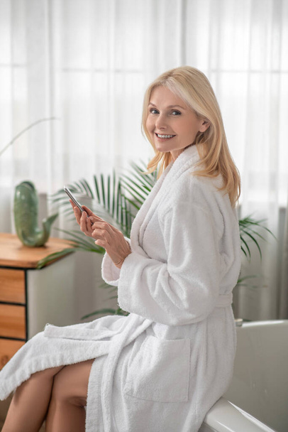 A woman in a white bath robe texting on a smartphone - Fotografie, Obrázek
