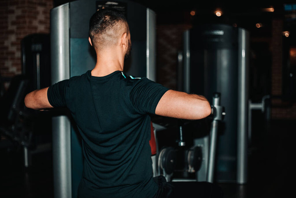 Low angle shot of a strong young fit and toned muscular athletic man doing exercise using crossover machine in gym. Sports fitness motivation strength concept. - Valokuva, kuva