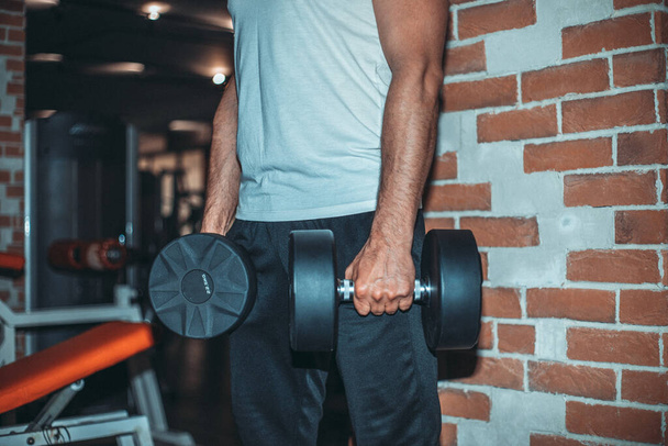 jovem fisiculturista fazendo exercício com halteres pesados no ginásio escuro. - Foto, Imagem