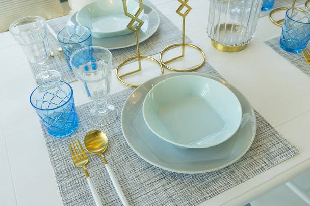 Pale green plate setting with gold fork and spoon on table. Dinning table with decorated vase and candle holder. - Fotó, kép