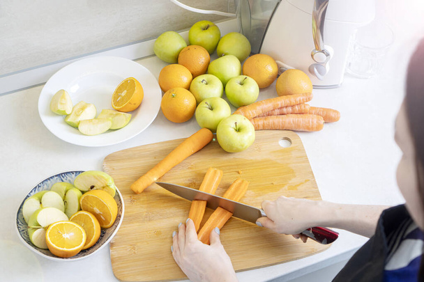 Woman prepares homemade fresh juice made with apples, oranges and carrots. - Photo, Image
