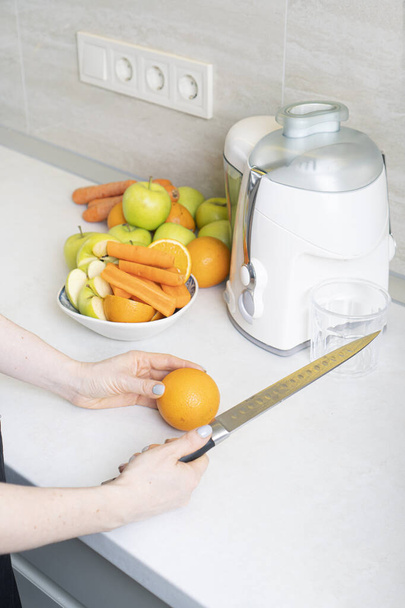 Girl prepares homemade fresh juice made with apples, oranges and carrots. Vertical photo. - Foto, Imagen