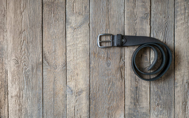Twisted black male leather belt on a wooden background. Copy space. - Фото, изображение