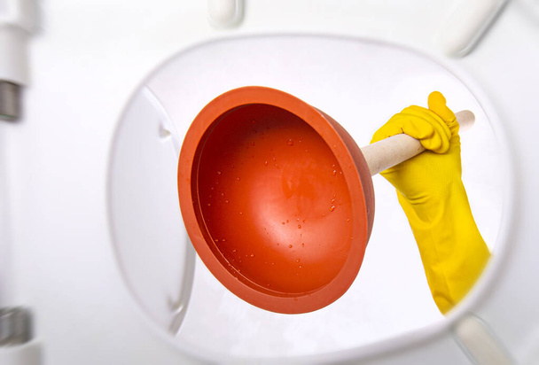 Cleaning the toilet with a plunger. Bathroom toilet plunger suction in a hand gets in the toilet. View from inside. - Photo, image