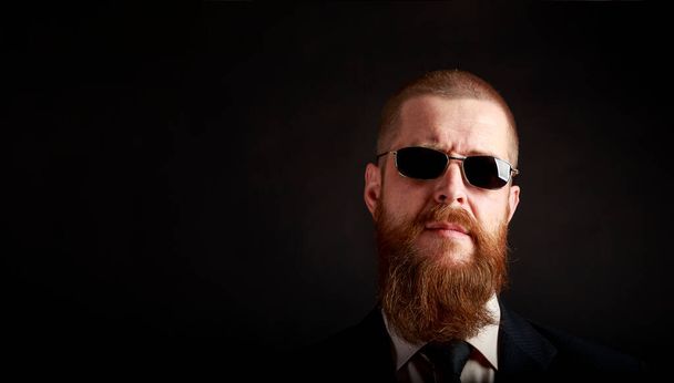 retrato de un hombre barbudo gafas de sol habitación oscura - Foto, Imagen