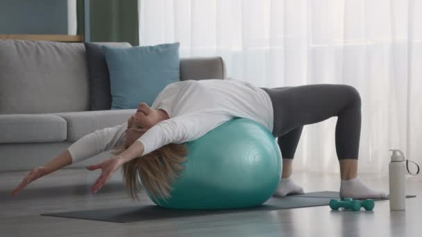 Femme plus âgée faisant Pilates exercice d'étirement allongé sur Fitball intérieur - Séquence, vidéo
