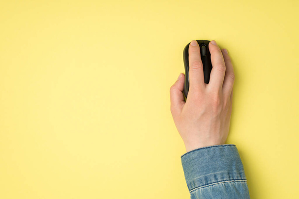 Foto in prima persona vista dall'alto di mano femminile con mouse senza fili computer nero su sfondo giallo isolato con copyspace - Foto, immagini