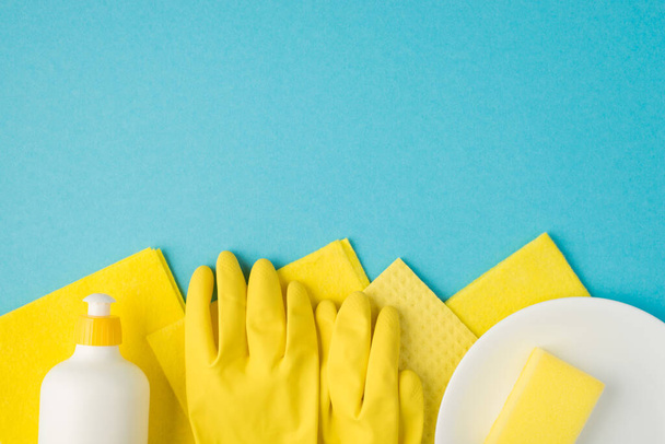 Overhead photo of soap cleaning rags yellow gloves and plate isolated on the blue background - Photo, Image
