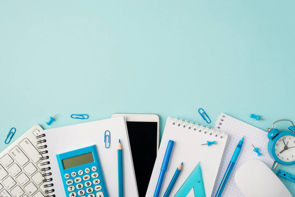 Foto von oben von blauen Schreibwaren-Heften Tastatur-Maus-Taschenrechner Bleistifte Lineal Wecker Smartphone-Pins und Clips auf isoliertem pastellblauem Hintergrund mit Leerraum - Foto, Bild