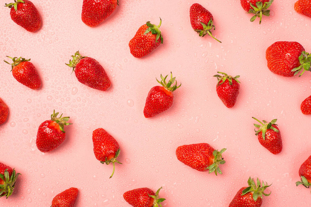 Foto de vista superior de fresas y gotas de agua sobre fondo rosa pastel aislado - Foto, Imagen