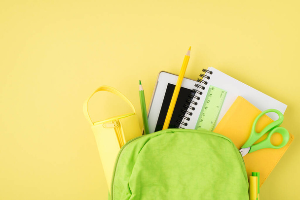 Overhead photo of backpack ruler notepad pen pencil tablet and pencil-case isolated on the yellow background - Фото, изображение