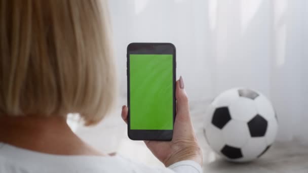 Deportiva mujer mayor sosteniendo el teléfono con pantalla verde interior, vista trasera - Imágenes, Vídeo