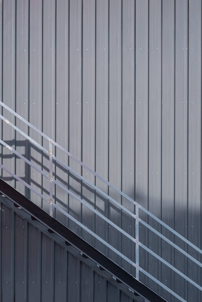 Tamamlanmamış inşaat alanındaki deponun gri kıvrımlı çelik duvarındaki metal merdiven ve tırabzan. - Fotoğraf, Görsel