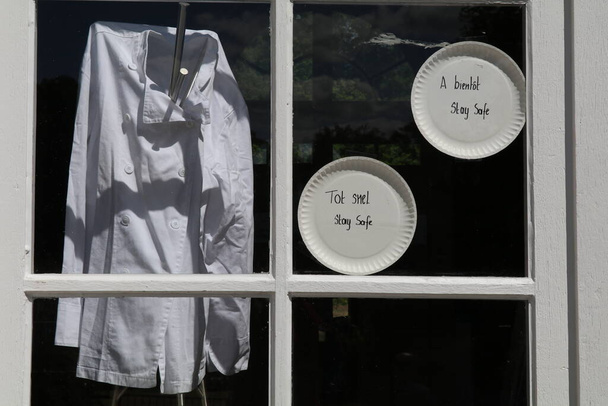 chef's jacket and signs in the window due forced closure of restaurants as safety measure to fight corona virus. Text reads "see you soon, stay safe" - Photo, Image