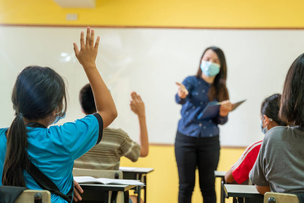 Aziatische leraar en de achterkant van de student met een les met gezichtsmasker terug op school na covid-19 quarantaine en lockdown. - Foto, afbeelding