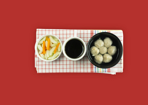 Fleischbällchensuppe serviert in einer weißen runden Schüssel und eingelegter Karottengurke auf rotem Hintergrund. - Foto, Bild