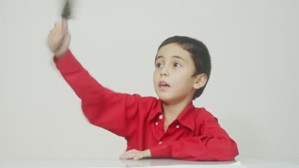 Little boy in the red long-sleeved shirt sat, combing his hair and talking all the time.studio shot white background.high quality video 4K.  - Footage, Video