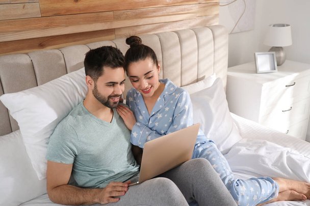 Happy couple in pajamas with laptop on bed at home - Foto, Imagen