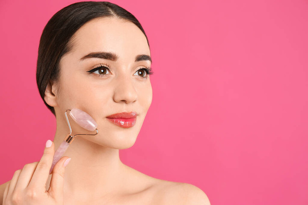 Woman using natural face roller on pink background, space for text - Foto, Imagen