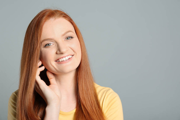 Candid portrait of happy young woman with charming smile and gorgeous red hair on light grey background, space for text - 写真・画像
