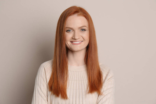 Candid portrait of happy young woman with charming smile and gorgeous red hair on beige background - Valokuva, kuva