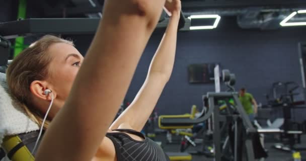 Cropped view of the strong woman squeezes heavy weight and training her arms at the gym while having power training at the special machine. Sport and workout concept - Materiał filmowy, wideo