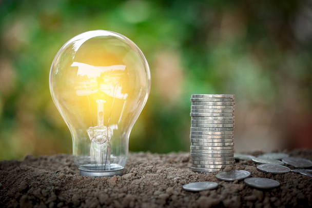 Light bulb and money stacking of coins for new concept, saving money, save energy concept put on the soil in soft green nature background. - Photo, Image