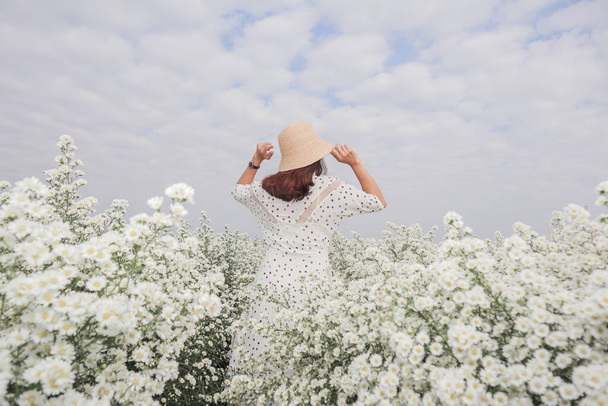Een vrouw in een vintage jurk strekt zich uit in het witte bloemenveld in de ochtend na het wakker worden. Jonge toeristen wandelen door een mooi en uitgestrekt wit bloemenveld om te ontspannen. - Foto, afbeelding