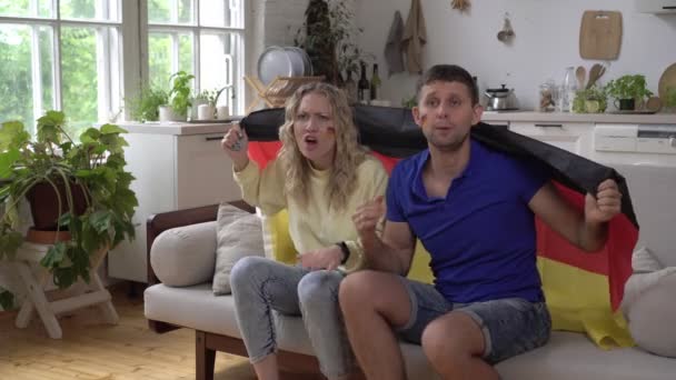 Οικογενειακό ζευγάρι των αθλητικών ή ποδοσφαιρικών οπαδών στο σπίτι με τη σημαία της Γερμανίας. Γερμανοί φίλαθλοι βλέπουν τηλεόραση στο σπίτι στον καναπέ - Πλάνα, βίντεο
