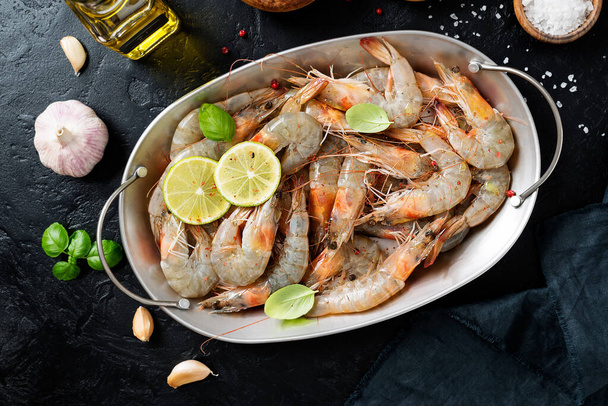 Crevettes crues fraîches marinées avec des épices et du jus de lime, prêtes à rôtir. Fond noir. Vue du dessus - Photo, image
