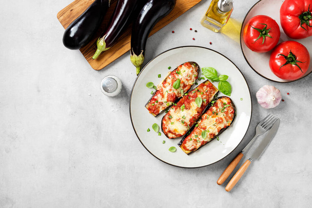 Gebakken aubergine met mozzarella kaas, gehakte tomaten en verse basilicumbladeren. Vegetarisch recept. Lichtgrijze achtergrond, bovenaanzicht. Ruimte voor tekst. - Foto, afbeelding