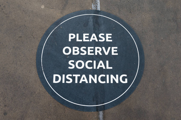 Ein Schild am Boden fordert die Menschen auf, soziale Distanzierungsregeln zu beachten. - Foto, Bild