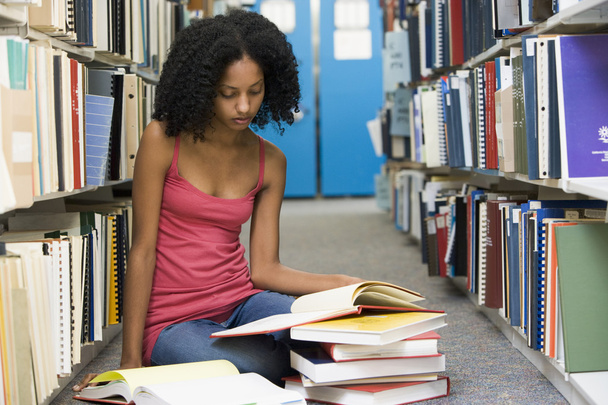 Female student sitting on library floor surrounded by books - Photo, image