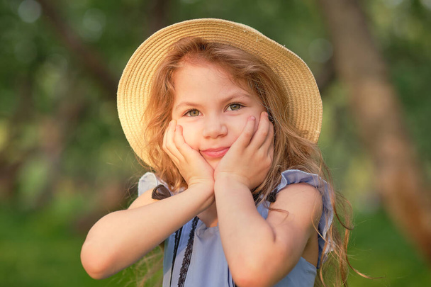 portrait of a young smiling girl, beautiful child outside in a straw hat enjoying a warm day - Photo, Image
